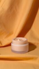 A jar of luxurious face cream sits on an orange fabric backdrop, ready to be used. The soft lighting enhances the creamy texture, suggesting a sense of pampering and self-care. 