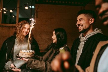 Friends celebrate together at a lively birthday gathering featuring a cake with a sparkler at night
