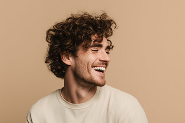Portrait of a cheerful young man with curly hair laughing with closed eyes isolated over beige background