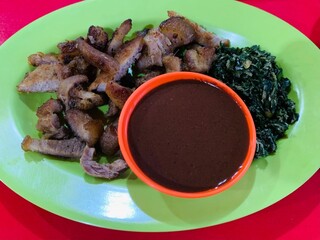 Close up babi panggang or roast pork, blood sauce and stir-fried cassava leaves on a plate. Delicious and tasty food