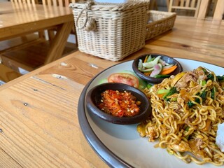 Mie or Bakmi or Noodle with tomato, pickles and chili sauce served on the plate on the table. Look...