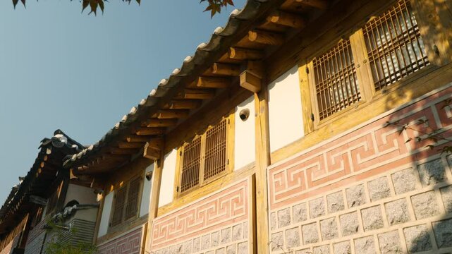 Low angle view of intricate wooden eaves, tiled roof, and patterned stone wall of a hanok in Bukchon Hanok Village, Jongno-gu, Seoul - revealing out of tree branches