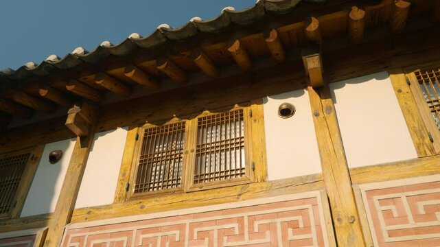 Sunlight reflects on wooden lattice windows beneath a tiled roof of a hanok in Bukchon Hanok Village, Jongno-gu, Seoul. Low angle shot