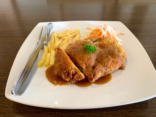 Close up of chicken cordon bleu on white plate, with french fries and salad. Delicious and tasty