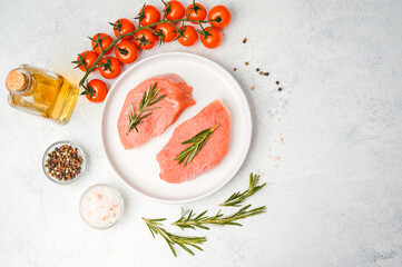 Two raw veal steaks with rosemary on white plate surrounded by cooking spices and vegetables