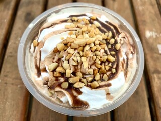 Close up a cup of vanilla ice cream with caramel syrup and peanut crumbs on the top. Sweet. cold, and delicious ice cream