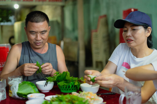 Group enjoys traditional Vietnamese cuisine while preparing fresh ingredients in a bustling street market at dusk in Hanoi