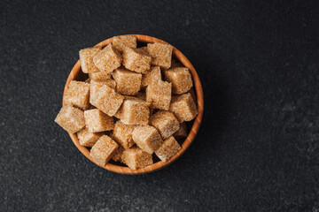 Brown sugar cubes arranged neatly in a wooden bowl on a dark surface