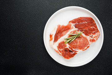 Uncooked beef steaks on white plate with rosemary and spices