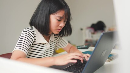 Asian teenage girl attentively watching an online class on a laptop at home, representing focused digital learning, homeschool, and remote education in a calm study space.