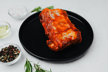 Spicy pork ribs on black plate with seasoning and herbs