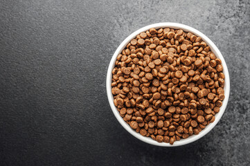 White bowl with dry dog food on dark gray background