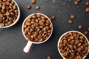 Three bowls of dry dog food on black textured background with scattered kibble