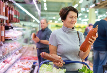 Elderly woman chooses sausage in supermarket