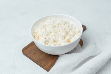 Freshly prepared cottage cheese in a bowl on a wooden cutting board