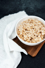 Healthy breakfast bowl of oatmeal on wooden board with white cloth