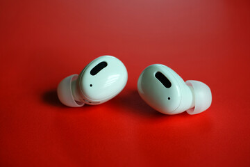 White wireless earbuds with silicone tips displayed on a vibrant red surface, showcasing modern design and compact features

