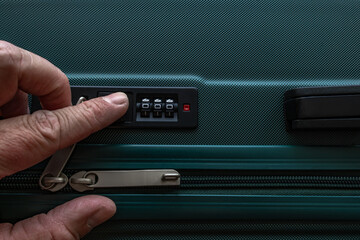 A man's hand on the combination lock of a suitcase,