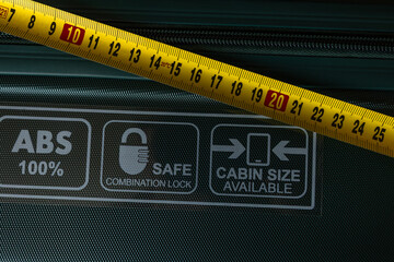 Yellow measuring tape placed on a suitcase, checking the correct size of luggage during airport...