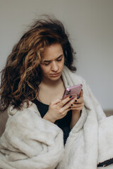 Woman Relaxing With Phone Under Blanket in Comforting Atmosphere