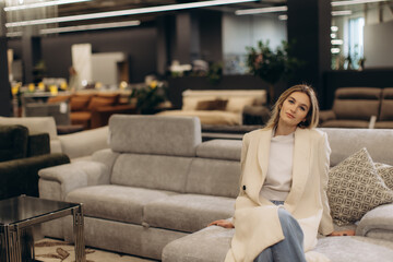 Obraz premium Young Woman Relaxing on Stylish Sofa in Modern Furniture Store