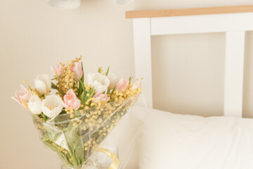 Bouquet of pink and white tulips with mimosa in a glass vase in a bedroom. Spring flower arrangement for interior decoration.