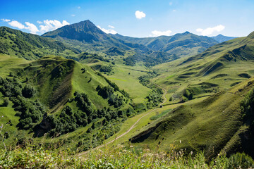Scenic views on mountain and valley at summer. Green meadows and forests, slopes, hilly countryside, blue sky with clouds. Beautiful landscape, travel background, wallpapers and banner.
