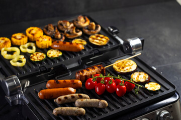 Electric grill cooking sausages, vegetables and mushrooms simultaneously