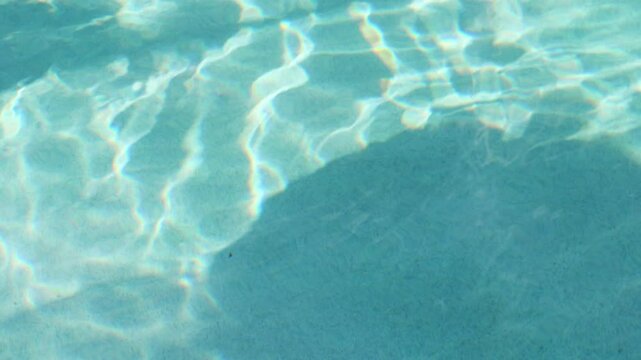 Rippling pool water with the shadows of pool toys moving overhead