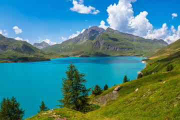 The vibrant turquoise waters of Lac du Mont Cenis are framed by green slopes and mountains of the French Alps.