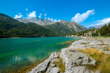 View of the Ceresole Reale lake and mountains under blue sky with white clouds in Piedmont, Italy.