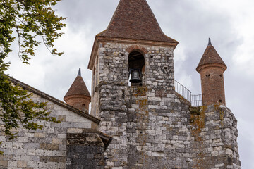Church bell tower with conical roofs in Auvillar, France, showing stone walls and cloudy sky