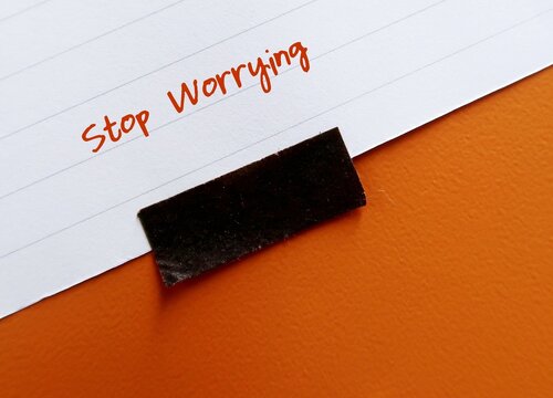 Stick note on orange background with text written STOP WORRYING - self talk to turn off anxious thoughts - to stay calm and look at life from less fearful perspective - reduce rumination