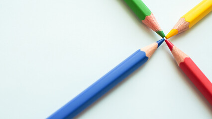 Minimalist composition featuring four colored pencils (green, yellow, blue, red) converging at...