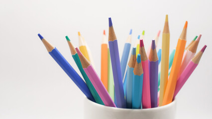 Fototapeta premium A collection of multicolored pencils arranged in a white ceramic cup against a bright, clean background
