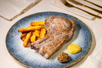 Grilled pork chop served with french fries and mustard on elegant blue plate