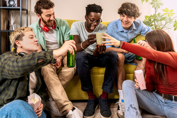 Five multicultural friends sharing coffee and popcorn snacks in a cheerful living room gathering