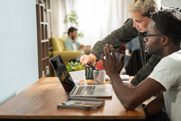 Black and female coworkers pointing at laptop screen together during collaborative home office work...