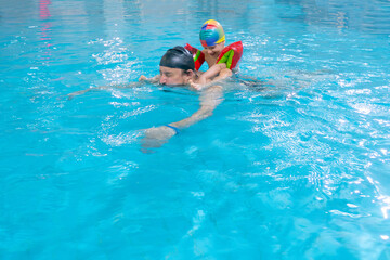Happy middle-aged father swimming with cute adorable baby in swimming pool. Smiling dad and little child, boy having fun together. Active family spending leisure and time in spa hotel. Concept of kids