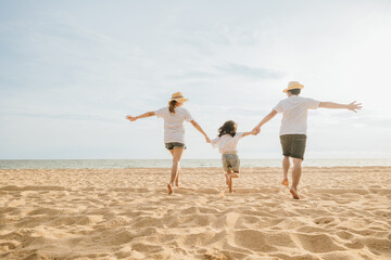 Happy Asian parents with their daughters enjoying playful at beach. Little girls with their mother and father holding hand of child running and pretending on sand. Positive family outdoor activity