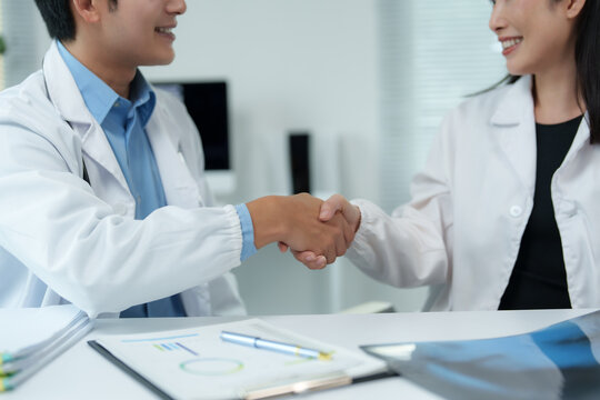 Two smiling asian doctors shaking hands after successful meeting in hospital office