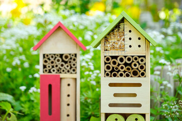 Two insect hotels or bee hotels in a summer garden with flowers. An insect hotel is a manmade structure created to provide shelter for insects in a variety of shapes and sizes and materials.	