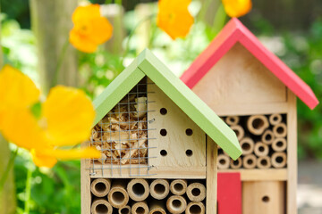 Two insect hotels or bee hotels in a summer garden with flowers. An insect hotel is a manmade structure created to provide shelter for insects in a variety of shapes and sizes and materials.	