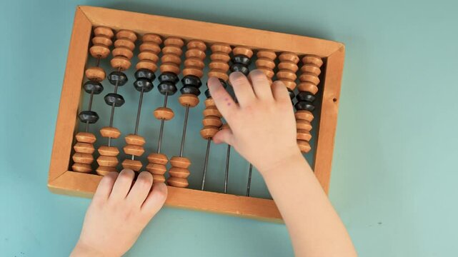 Little child's hands hold wooden abacus on a blue background. Close up, point of view shot. View from above.
