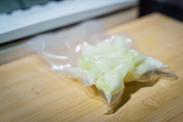 Sealer for vacuum packing with plastic bag of Onion, cut crosswise on wooden table, flat lay, top view.