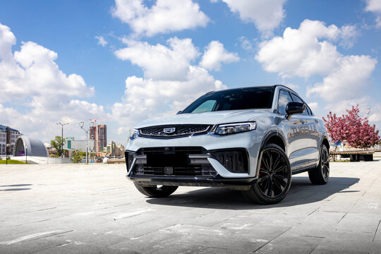 Geely Tugella SUV logo detail parked in a city with blue sky and buildings in the background High-quality photography