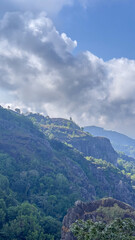 Serene Mountain Landscape Under a Cloudy Sky: Breathtaking View of Lush Green Hills and Steep Cliffs