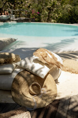 Straw hat and boho-style pillows by the poolside in tropical sunlight. Relaxing summer setup with calm holiday vibes.