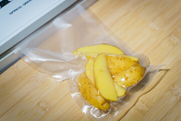 Sealer for vacuum packing with plastic bag of potato on wooden table, flat lay, top view.