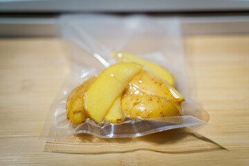Sealer for vacuum packing with plastic bag of potato on wooden table, flat lay, top view.